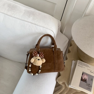 Detail of a brown suede Boston bag featuring embossed logo and a cute plush bear pendant