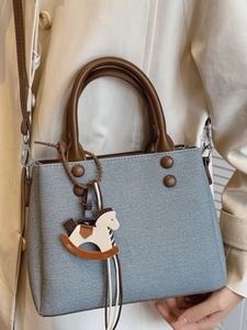 Chic grey tote bag with brown leather handles and rocking horse charm on beige coat