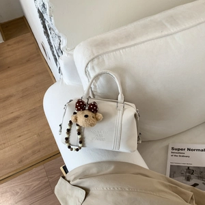 Detailed view of white Boston bag with embossed logo, plush bear and beaded charms