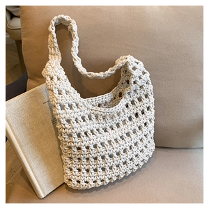 Detailed macro view of cream hand-woven mesh hollow hobo bag on a soft fabric sofa