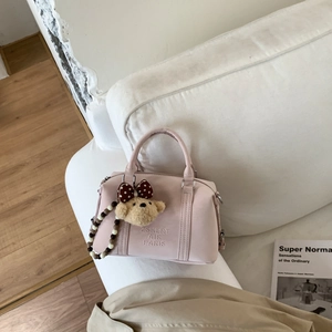 Detail of light pink Boston bag with plush bear charm and beaded strap on white sofa