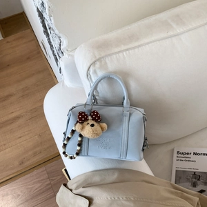 Close-up of light blue leather Boston bag with plush bear charm on a white sofa