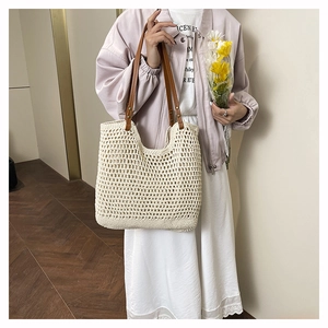 Detail of hand-woven off-white tote bag featuring brown leather handles and hollow mesh texture