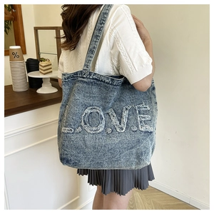 Detailed view of the frayed LOVE embroidery on a blue vintage denim tote bag