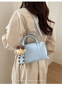 Detail of light blue Boston bag featuring embossed logo text and a cute bear charm