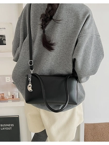 Rear view of a model wearing a minimalist black rectangular shoulder bag with silver charm