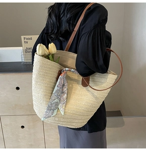 Close-up of woven straw tote bag with brown leather strap and decorative green silk scarf