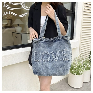 Outdoor model shot showing the large denim tote bag with frayed L.O.V.E. embroidery detail