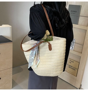 Detail of a straw tote bag with brown leather handles and decorative floral silk scarf