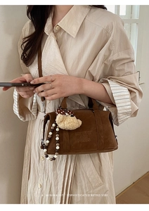 Detail of retro suede Boston bag with plush bear charm and brand logo embossing