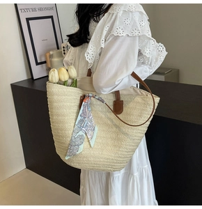 Detail of handwoven straw tote bag featuring floral scarf and leather straps for summer beach