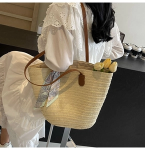 Detail of hollow woven straw tote bag with brown faux leather handles and floral scarf