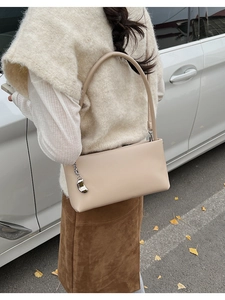 Street style view of a beige leather baguette bag with a silver metallic charm detail
