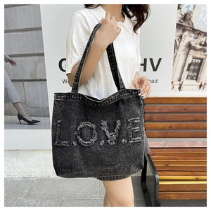 Close-up of black washed denim tote bag featuring frayed LOVE letters and metal studs