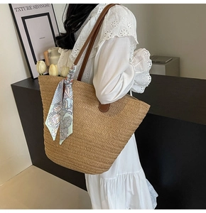 Close-up of woven straw tote bag with brown leather straps and vintage floral silk scarf