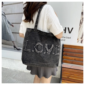 Detailed close-up of dark grey washed denim tote bag featuring frayed 'LOVE' letter patches