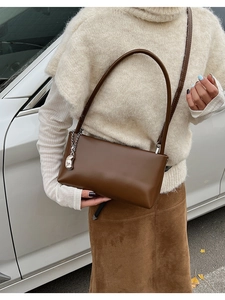 Detail of chocolate brown leather baguette bag with silver bean charm on shoulder strap