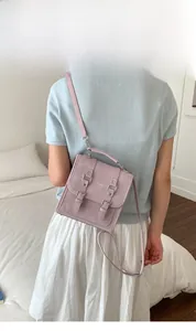 Pink square crossbody bag in faux suede with metal buckle straps shown on model