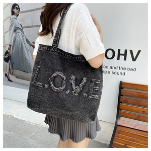 Macro view of the large denim tote bag featuring frayed 'LOVE' letter embroidery details