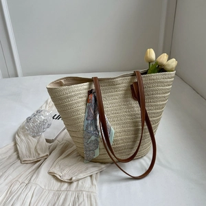 Detailed close-up of straw woven tote bag with leather handles and decorative silk scarf