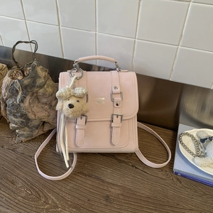 Close-up of pink PU leather mini backpack with silver buckles and a cute plush dog charm
