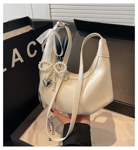 White hobo shoulder bag detail featuring elegant lace bow and pearl heart pendant charm.