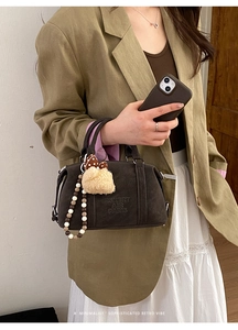Detailed macro of dark coffee Boston bag with embossed logo and fuzzy plush charm