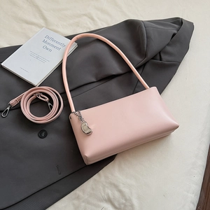 Detailed view of pink leather baguette bag with silver bean charm on a gray suit background