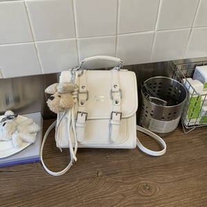 Close-up of white minimalist square crossbody bag with a cute plush dog charm accessory