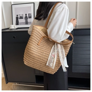 Dettaglio borsa a secchiello in paglia intrecciata con manici in pelle e foulard