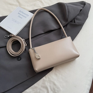 Detailed macro view of beige baguette bag with metallic charm and adjustable strap