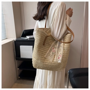 Dettaglio della borsa in paglia intrecciata con pizzo bianco e ricami floreali rosa