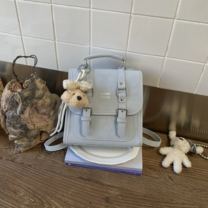 Close-up of a light blue square bag with metal buckles and a cute teddy bear charm