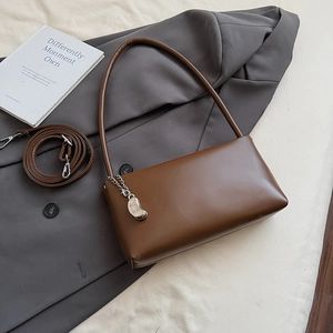 Detail of a brown leather baguette bag worn over a grey blazer for a retro aesthetic