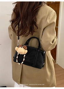 Detail of black suede Boston bag with embossed text, pearl chain, and plush bear charm