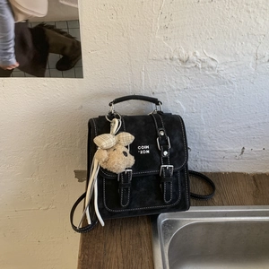 Detail of black faux suede crossbody bag with white stitching and bear charm accessory