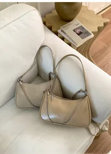 Détail de sacs bandoulière en cuir crème et kaki avec chaînes sur un canapé