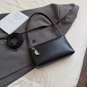 Detail of black matte leather baguette bag with silver bean charm on a grey blazer