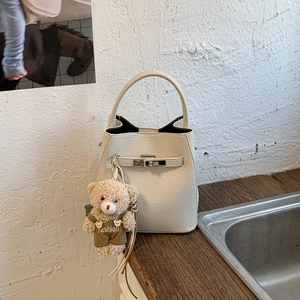 Detail of off-white lychee leather bucket bag with silver clasp and teddy bear charm