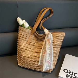 Dettaglio della borsa in paglia intrecciata con foulard di pizzo e manici in pelle