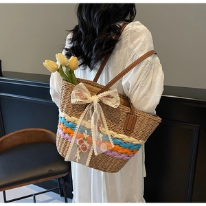 Detail of hand-woven straw tote bag with colorful stripes and white lace flower bow