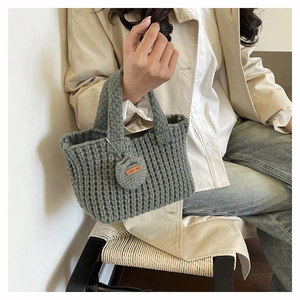 Detail shot of a grey handmade knit handbag with a heart-shaped tag on a light trench coat