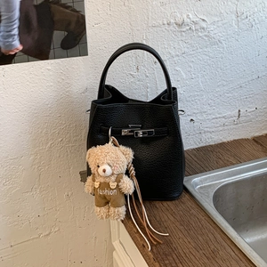 Close-up of black litchi leather bucket bag featuring a silver lock and cute bear charm