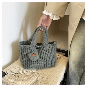 Detailed close-up of grey knitted handbag texture with a Hand Made leather label