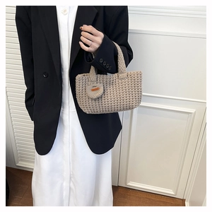 Close-up of hand-woven beige tote bag featuring a leather Hand Made tag and round charm