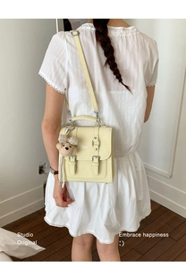 Detail of light yellow satchel bag with cute teddy bear charm and adjustable shoulder strap