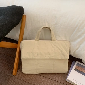 Detailed view of beige quilted laptop bag with padded handle on wooden floor