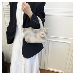 Detail of hand-knitted beige shoulder bag with crochet texture and orange leather label