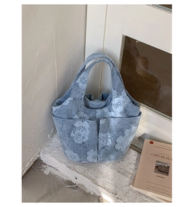 Detail of light blue floral denim tote bag showing functional front pockets and fabric texture