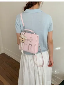 Pink matte leather messenger bag with plush bear charm worn by model in casual style